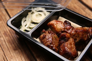 Photo of Plastic container of tasty shish kebab on wooden table, closeup. Food delivery service