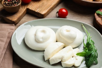 Photo of Delicious burrata cheese with arugula on wooden table, closeup