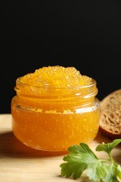 Photo of Fresh pike caviar in glass jar, bread and parsley on wooden board, closeup