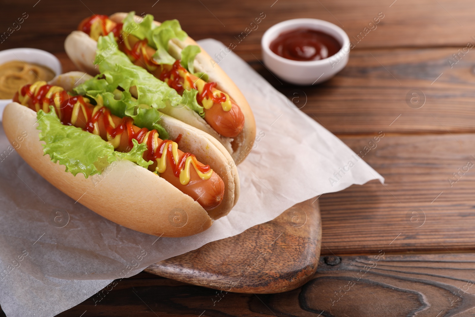 Photo of Tasty hot dogs with lettuce, ketchup and mustard on wooden table. Space for text