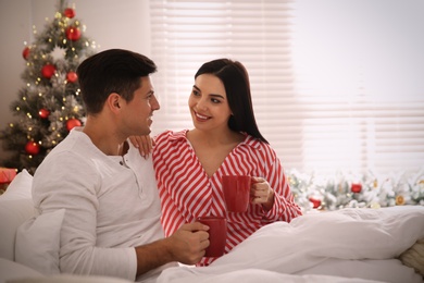 Happy couple with cups in bed. Christmas celebration