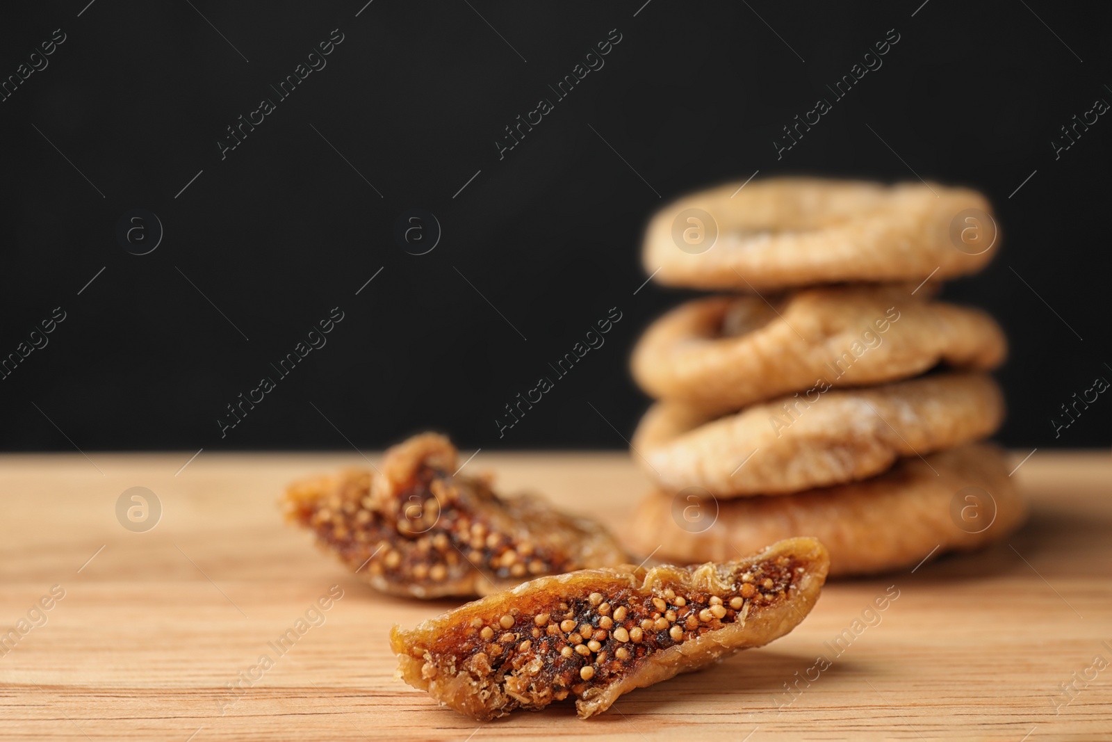 Photo of Tasty dried figs on wooden table against black background, closeup. Space for text