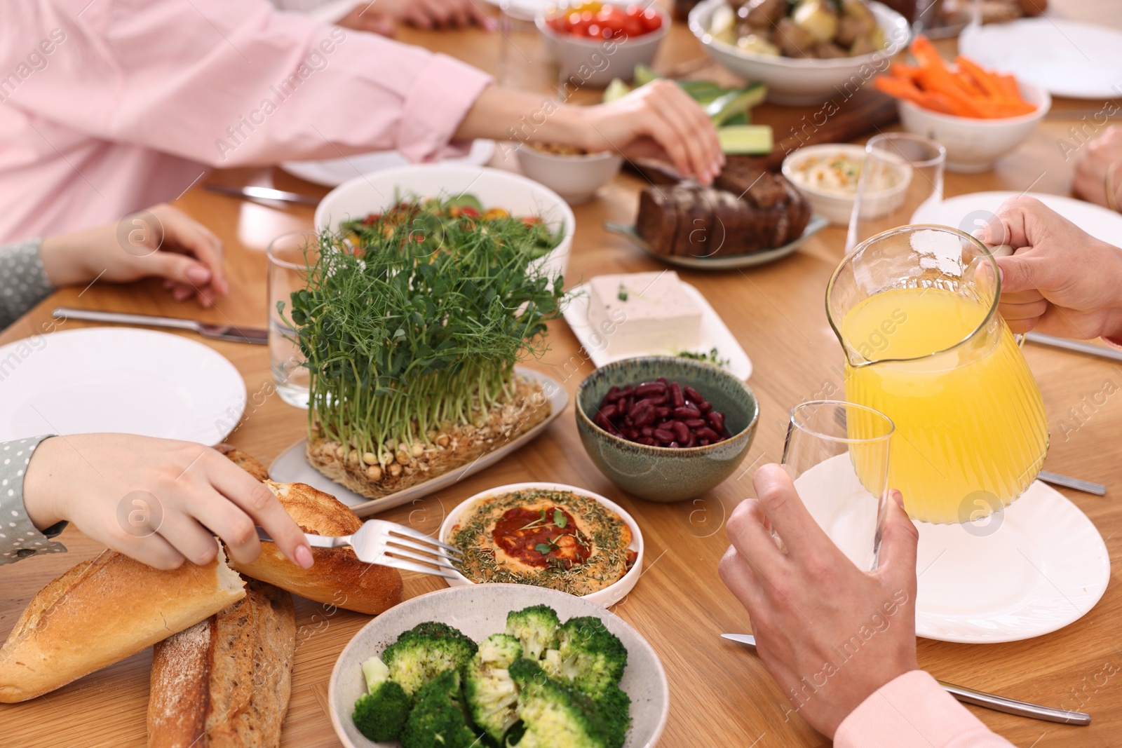 Photo of Friends eating vegetarian food at wooden table indoors, closeup