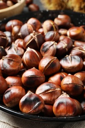 Photo of Delicious roasted edible chestnuts in frying pan on table, closeup