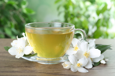 Photo of Cup of tea and fresh jasmine flowers on wooden table