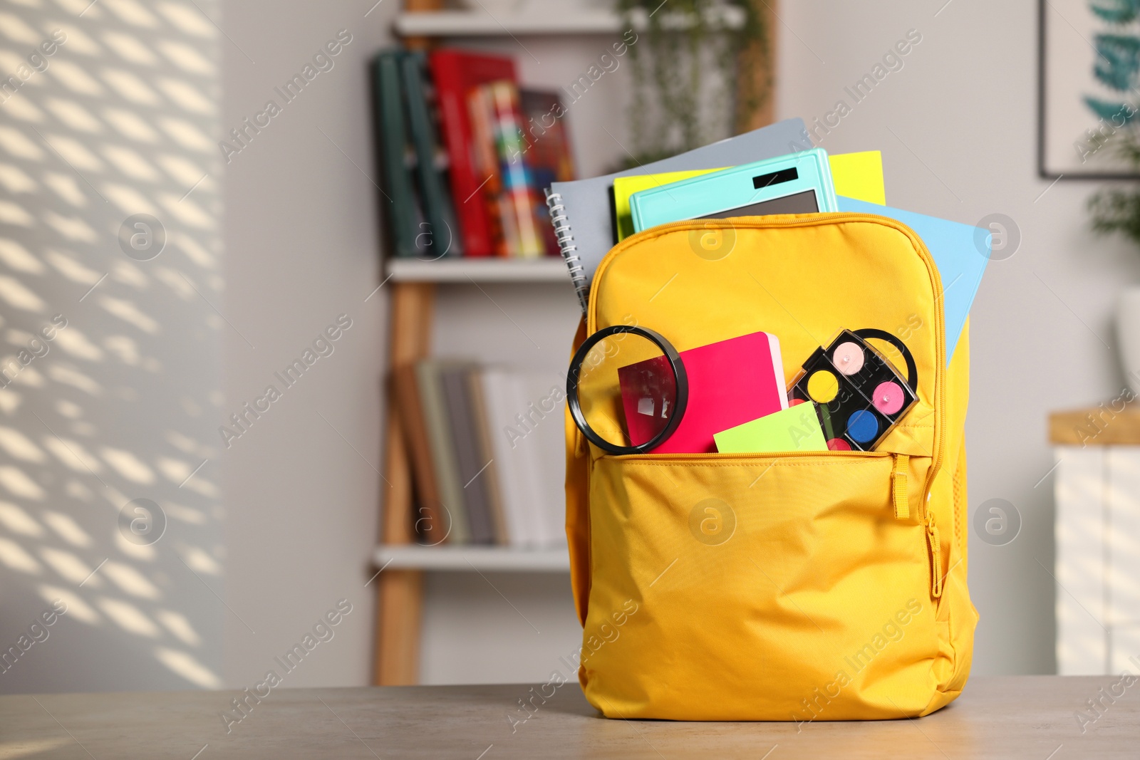 Photo of Yellow backpack with different school stationery on table indoors, space for text