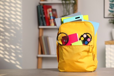 Yellow backpack with different school stationery on table indoors, space for text