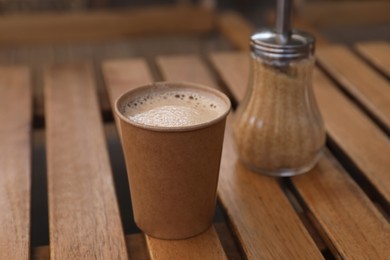 Photo of Takeaway paper cup with coffee near brown sugar on wooden table, closeup