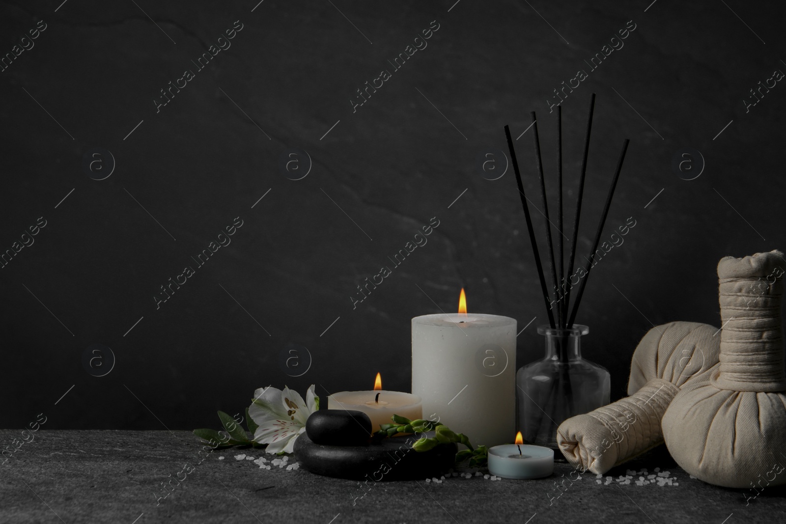 Photo of Beautiful spa composition with different care products and burning candles on dark grey table against black background. Space for text