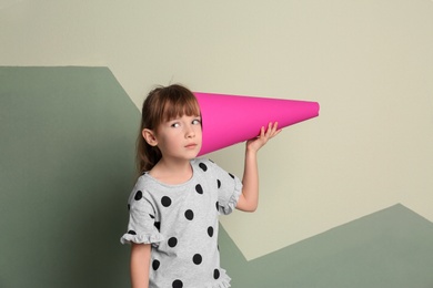 Cute little girl with paper megaphone on color background