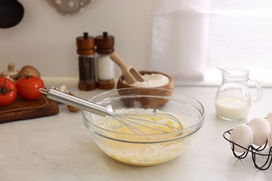 Metal whisk, cream in bowl and different products on light table indoors