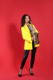 Beautiful African American woman playing saxophone on red background