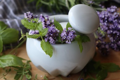 Mortar with fresh lavender flowers, mint and pestle on table, closeup