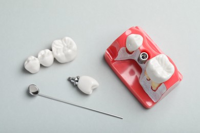 Educational model of gum with post between teeth, dental implant and mirror on grey background, above view