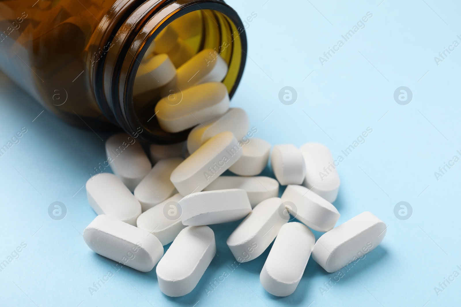 Photo of Bottle and vitamin capsules on light blue background, closeup