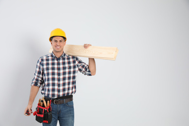 Photo of Handsome carpenter with wooden planks on light background. Space for text