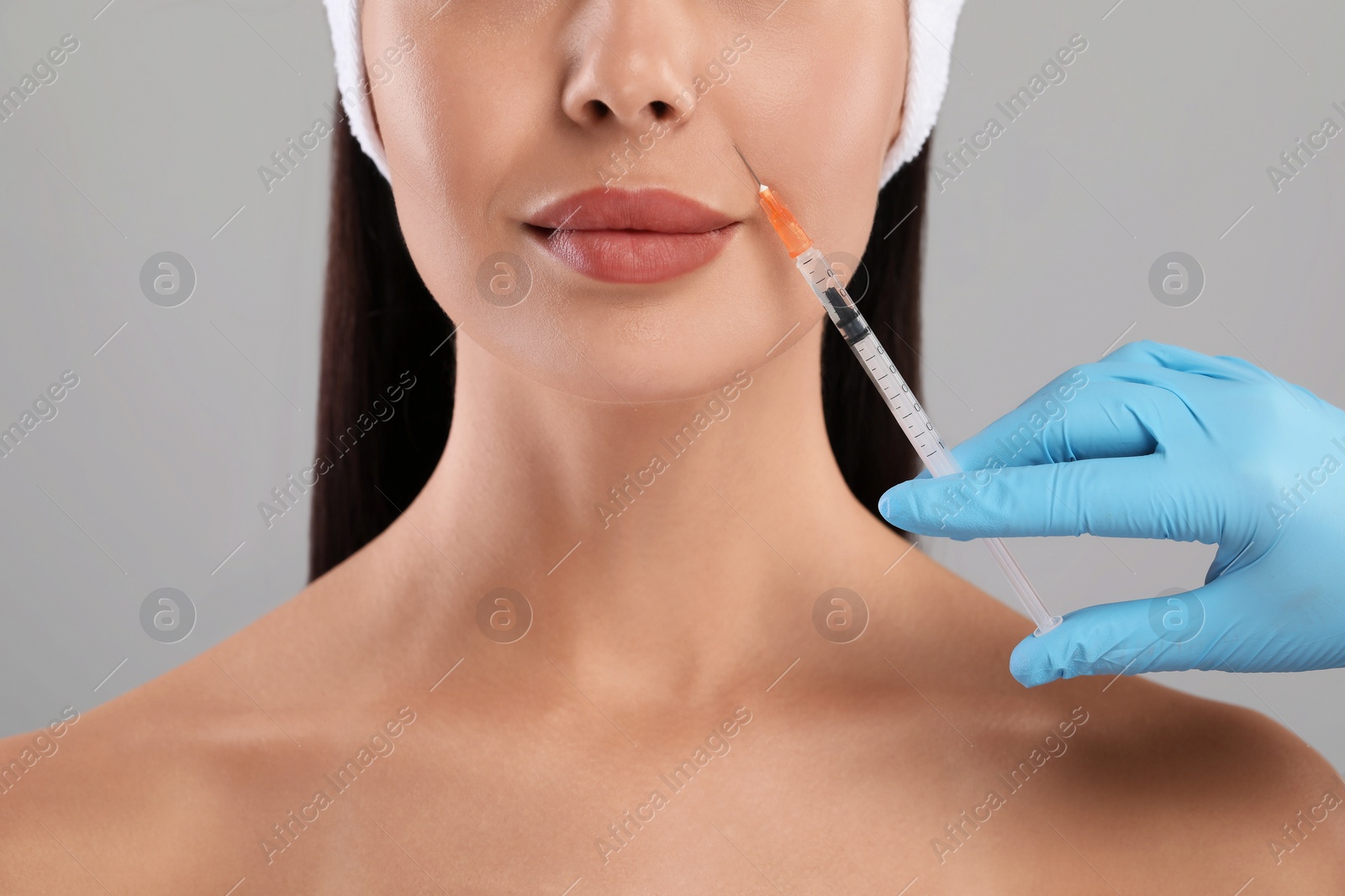 Photo of Doctor giving facial injection to young woman on light grey background, closeup. Cosmetic surgery