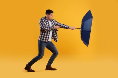 Photo of Emotional man with umbrella caught in gust of wind on yellow background