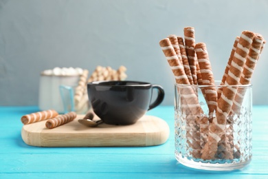 Photo of Glass with chocolate wafer rolls and cup of tea on wooden table