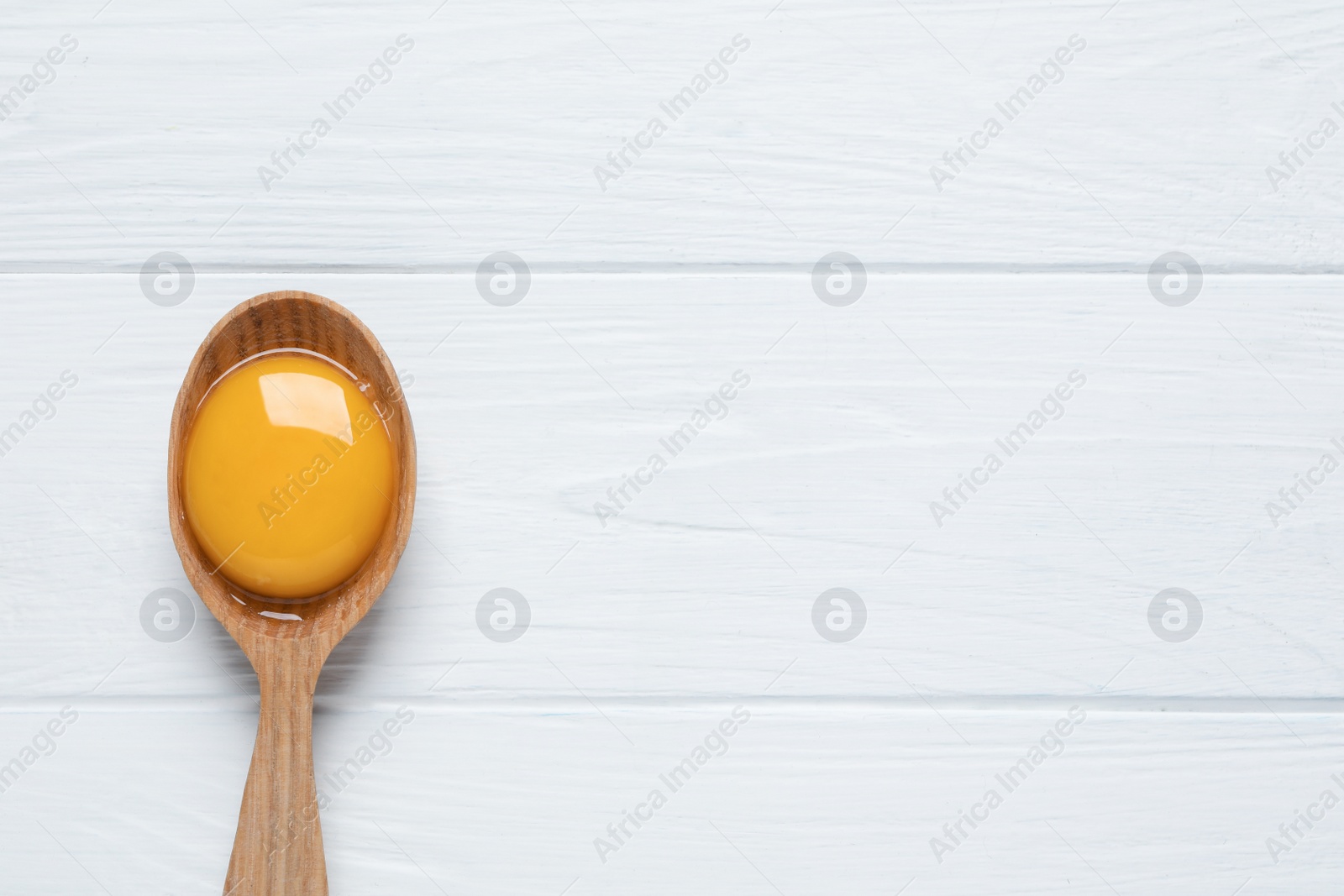 Photo of Spoon with raw egg yolk on white wooden table, top view. Space for text