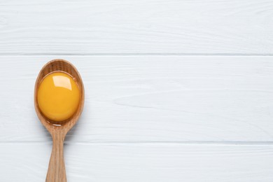 Photo of Spoon with raw egg yolk on white wooden table, top view. Space for text