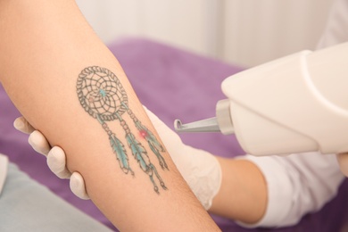 Photo of Young woman undergoing laser tattoo removal procedure in salon, closeup