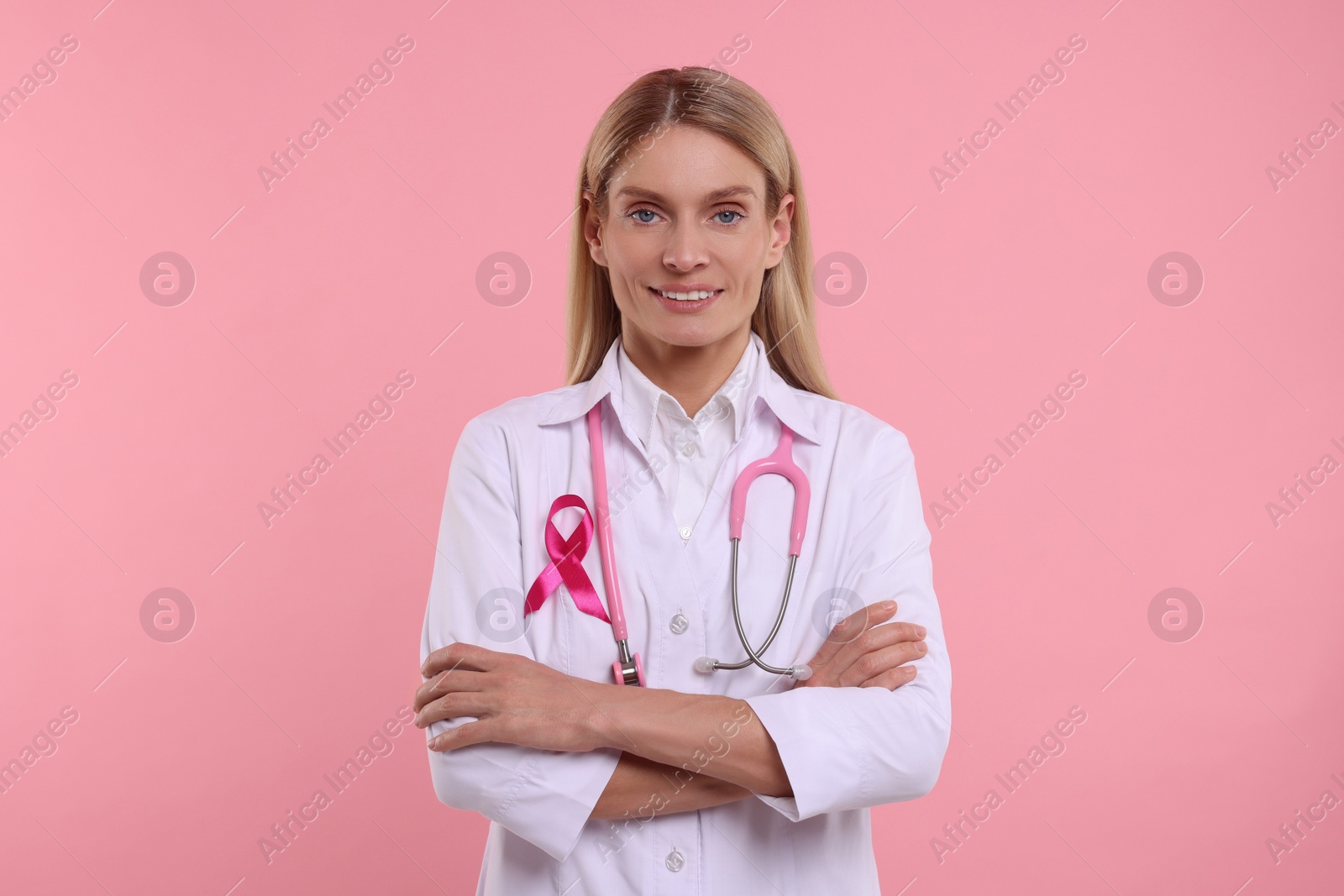 Photo of Doctor with pink ribbon and stethoscope on color background. Breast cancer awareness