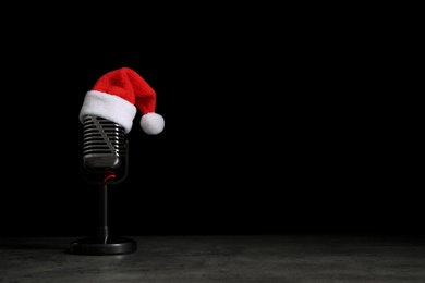 Microphone with Santa hat on grey stone table against black background, space for text. Christmas music