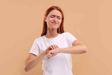 Photo of Suffering from allergy. Young woman scratching her arm on beige background