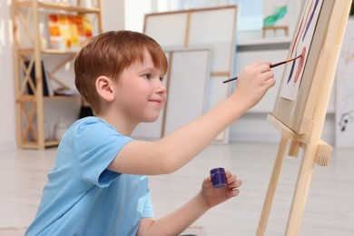 Photo of Little boy painting in studio. Using easel to hold canvas