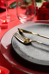 Place setting with heart shaped candles and bouquet of roses on red table, closeup. Romantic dinner