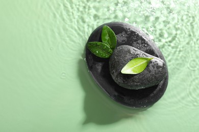 Photo of Spa stones and fresh leaves in water on light green background, top view. Space for text