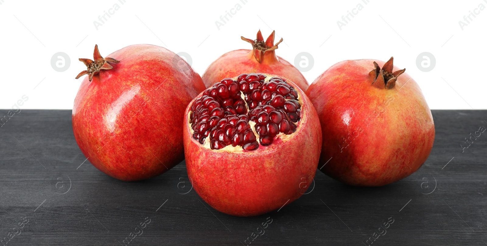 Photo of Fresh pomegranates on black wooden table against white background