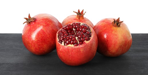 Fresh pomegranates on black wooden table against white background