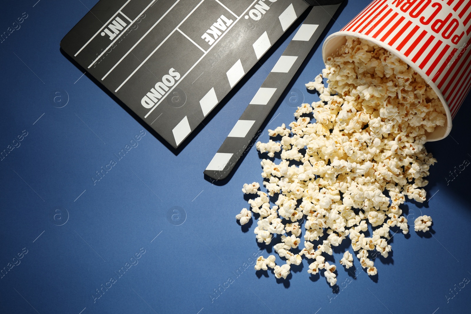 Photo of Delicious popcorn and clapperboard on blue background, above view
