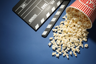 Photo of Delicious popcorn and clapperboard on blue background, above view