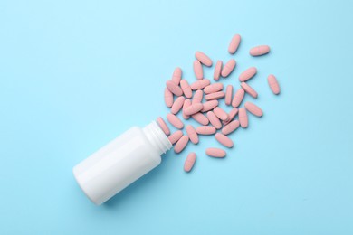 Vitamin pills and bottle on light blue background, top view