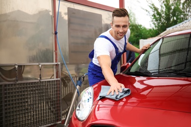 Male worker cleaning vehicle with cloth at car wash