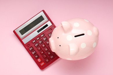 Calculator and piggy bank on pink background, top view