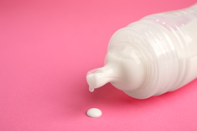 Photo of Feeding bottle with milk on pink background, closeup. Space for text