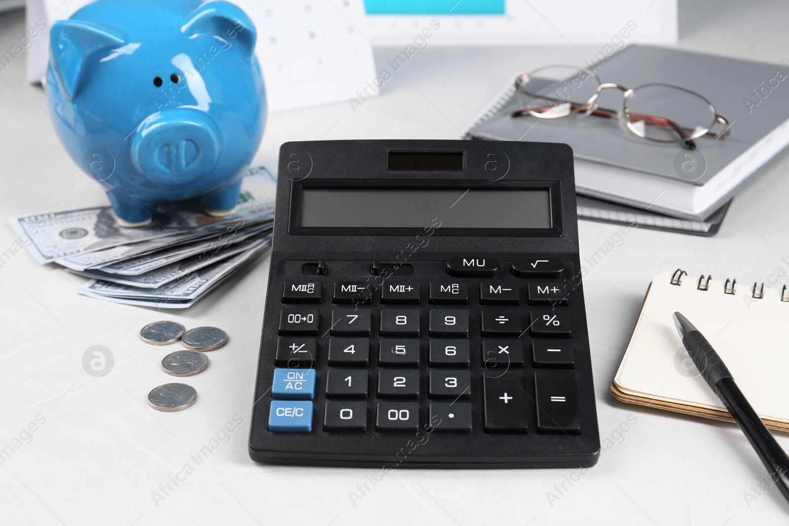 Photo of Calculator, piggy bank, money, glasses, pen and notebooks on white table. Pension planning