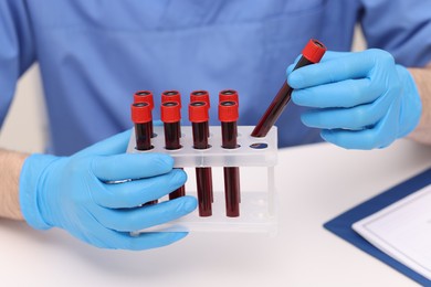 Photo of Doctor with samples of blood in test tubes at white table, closeup
