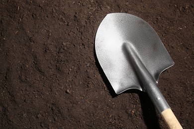 Photo of Metal shovel on fertile soil, top view and space for text. Gardening tool