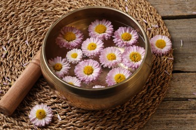 Photo of Tibetan singing bowl with water, chrysanthemum flowers and mallet on table