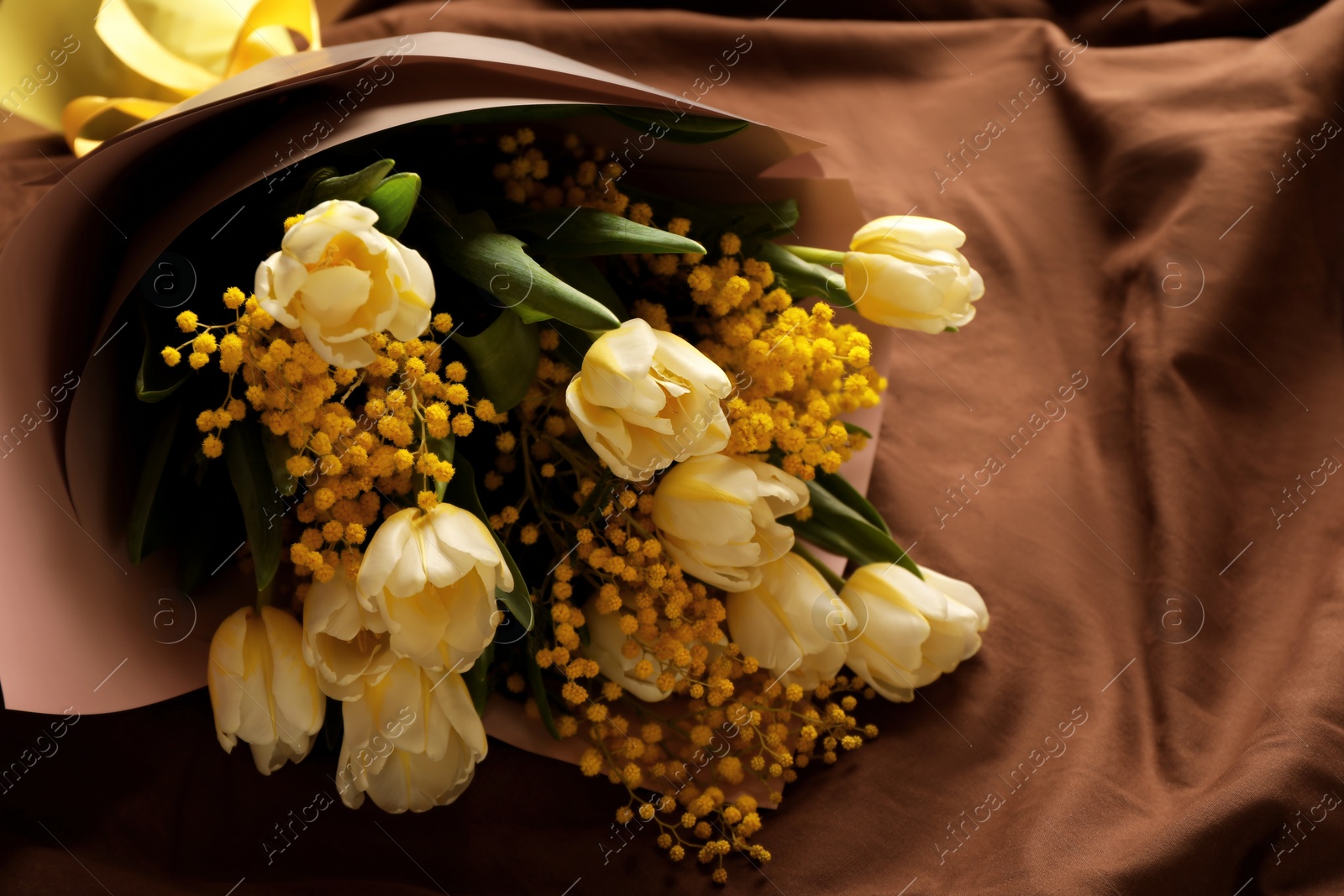 Photo of Bouquet of beautiful spring flowers on brown fabric, above view. Space for text