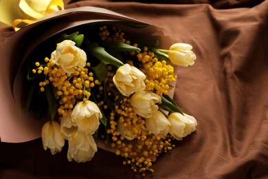 Photo of Bouquet of beautiful spring flowers on brown fabric, above view. Space for text