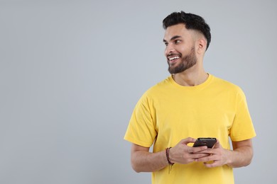 Photo of Happy young man using smartphone on grey background, space for text