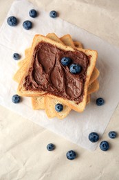 Photo of Tasty toast with chocolate paste and blueberries on parchment paper, flat lay