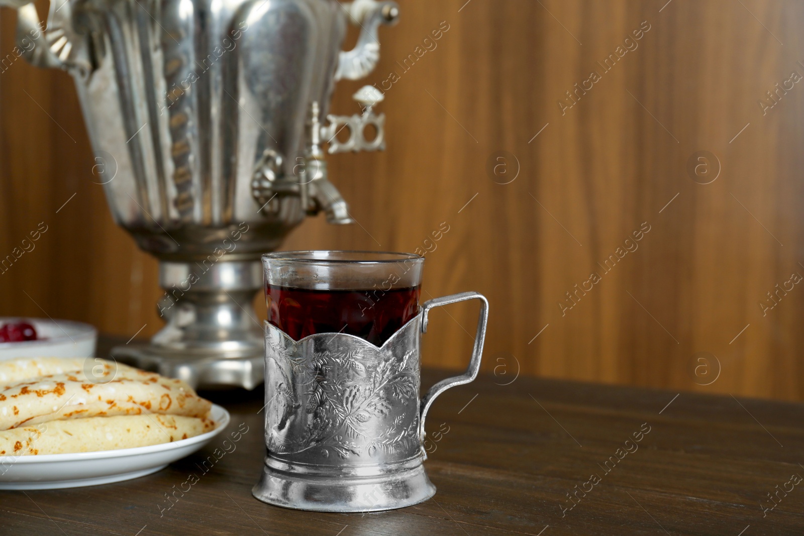 Photo of Vintage samovar, cup of hot drink and pancakes served on wooden table, space for text. Traditional Russian tea ceremony