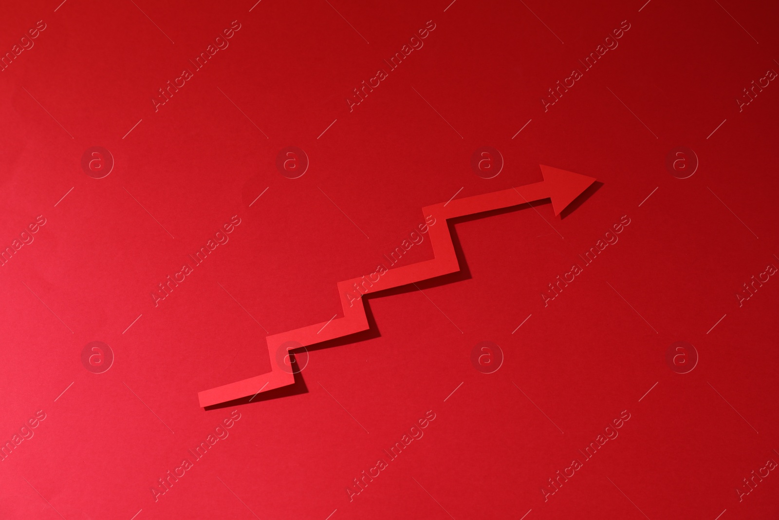 Photo of One zigzag paper arrow on red background, above view